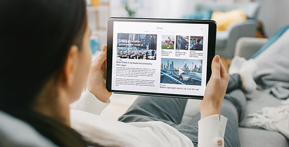 Une personne installée confortablement lis des articles d'actualité sur une tablette.