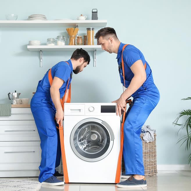 Deux livreurs installent une machine à laver dans  une salle de bain.