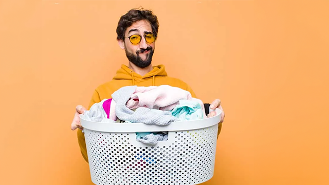 Homme avec des lunettes tenant un panier à linge dans les mains sur un fond jaune.