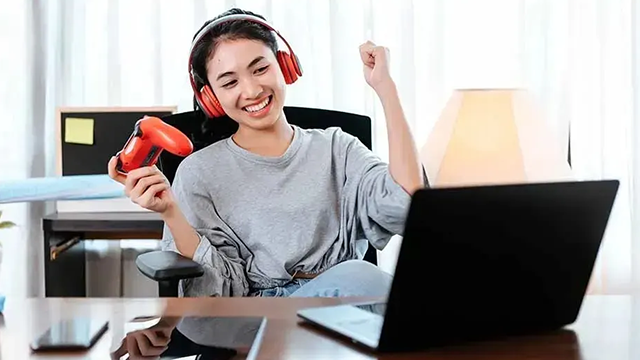 Une jeune fille qui avec une manette dans les mains et un casque sur les oreilles qui semble avoir remporté une partie de jeu vidéo.