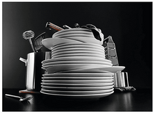 Charger l&#39;image dans la galerie, Une pile d&#39;assiettes blanches, d&#39;ustensiles et d&#39;autres outils de cuisine sur une surface noire.
