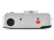 Charger l&#39;image dans la galerie, Vue latérale d&#39;un appareil photo argenté. Molette et bouton noirs, bouton rouge. Molette supérieure.
