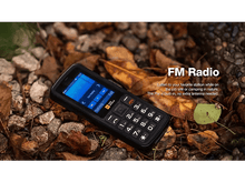 Charger l&#39;image dans la galerie, Un téléphone portable robuste avec fonction radio FM, posé sur un lit de feuilles et de brindilles.
