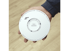 Charger l&#39;image dans la galerie, Une main tenant un détecteur de fumée et de monoxyde de carbone blanc. Étiquettes de test, silence et avertissement.
