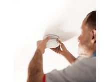 Charger l&#39;image dans la galerie, Homme installant un détecteur de fumée sur un plafond blanc. Mains tenant l&#39;appareil, arrière-plan flou.
