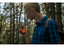 Charger l&#39;image dans la galerie, Homme dans une forêt tenant un talkie-walkie orange, avec un sac à dos.
