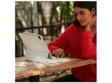 Charger l&#39;image dans la galerie, Femme en pull rouge utilisant une tablette blanche avec clavier, assise dehors à une table en bois.
