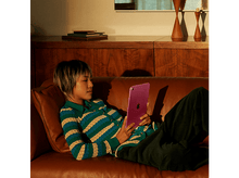 Charger l&#39;image dans la galerie, Femme sur un canapé marron tenant une tablette rose, portant une chemise rayée et un pantalon vert.
