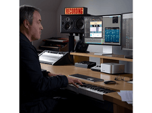 Charger l&#39;image dans la galerie, Un homme jouant d&#39;un clavier de piano dans un studio d&#39;enregistrement, avec des écrans d&#39;ordinateur.
