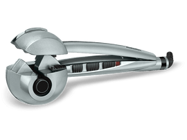 Fer à boucler Babyliss argenté. Il a une poignée noire et des boutons de commande. La chambre de bouclage est visible.