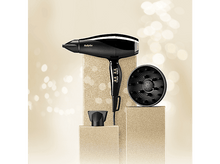 Charger l&#39;image dans la galerie, Un véhicule tout-terrain bleu dans un paysage avec des fleurs pourpres, des arbres et une structure en pierre.
