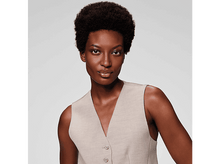 Charger l&#39;image dans la galerie, Une femme à la peau foncée et aux cheveux courts, foncés et bouclés. Elle porte un gilet beige et regarde la caméra.
