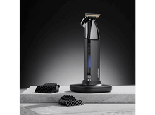 Charger l&#39;image dans la galerie, Une tondeuse à cheveux Babyliss noire et argentée avec deux accessoires de coupe noirs sur un socle.
