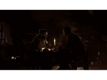 Charger l&#39;image dans la galerie, Deux hommes dans une pièce sombre, assis à une table avec des bougies. L&#39;un parle.
