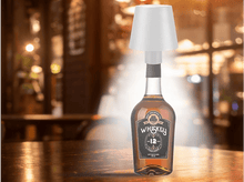 Charger l&#39;image dans la galerie, Une bouteille de whisky avec un abat-jour dessus, posée sur une table en bois dans un bar.
