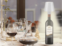 Charger l&#39;image dans la galerie, Bouteille de vin avec une lampe dessus, verres à vin et une carafe sur une table.
