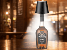 Charger l&#39;image dans la galerie, Bouteille de whisky avec abat-jour sur table en bois. Arrière-plan flou d&#39;un bar.
