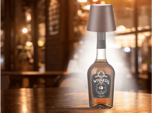 Charger l&#39;image dans la galerie, Bouteille de liqueur avec une lampe dessus, sur une table en bois dans un bar.
