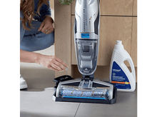 Charger l&#39;image dans la galerie, Une personne utilisant un aspirateur avec une bouteille blanche de solution de nettoyage à côté.
