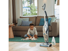 Charger l&#39;image dans la galerie, Un garçon caresse un chien sur un tapis vert, un aspirateur est à proximité dans le salon.
