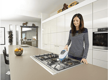 Charger l&#39;image dans la galerie, Femme nettoyant une table de cuisson avec un nettoyeur vapeur dans une cuisine moderne.
