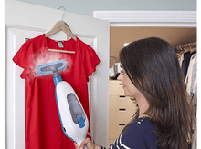 Charger l&#39;image dans la galerie, Une femme repassant à la vapeur un chemisier rouge suspendu à une porte. La vapeur est visible sur le chemisier.
