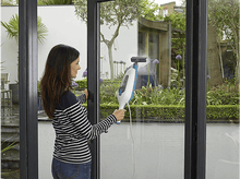 Charger l&#39;image dans la galerie, Femme nettoyant une fenêtre avec un nettoyeur vapeur. Elle porte une chemise rayée.

