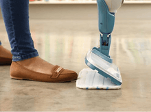 Charger l&#39;image dans la galerie, Pieds d&#39;une personne en chaussures marron et jean avec un balai vapeur en action sur un sol.
