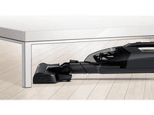 Charger l&#39;image dans la galerie, Tête d&#39;aspirateur noire sous une table blanche, sur un plancher en bois.
