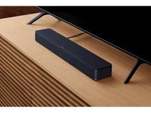 Charger l&#39;image dans la galerie, Une barre de son noire sur un meuble en bois. Un téléviseur noir au-dessus.
