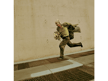 Charger l&#39;image dans la galerie, Un homme en vêtements verts courant avec des fleurs, à côté d&#39;un mur en béton.
