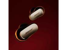 Charger l&#39;image dans la galerie, Deux écouteurs sans fil, noirs avec des accents dorés, sur fond rouge.
