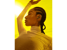 Charger l&#39;image dans la galerie, Une femme avec des tresses porte un haut blanc et des écouteurs. Fond jaune avec lumière du soleil vive.
