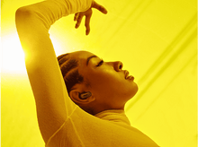 Charger l&#39;image dans la galerie, Femme avec écouteurs, bras levé, devant un fond jaune.
