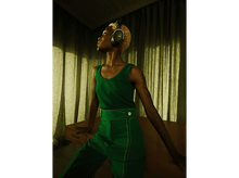 Charger l&#39;image dans la galerie, Femme en tenue verte avec casque, regardant en haut, appuyée sur un bureau.
