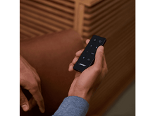 Charger l&#39;image dans la galerie, La main d&#39;une personne tenant une télécommande noire Bose. Le fond est marron.
