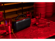 Charger l&#39;image dans la galerie, Un haut-parleur Bose noir sur une table rouge, avec de l&#39;eau et des verres autour.
