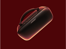 Charger l&#39;image dans la galerie, Un haut-parleur Bose noir avec une poignée, dans une prise de studio sur fond rouge foncé.
