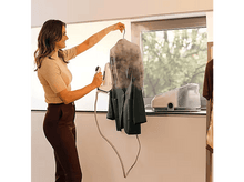 Charger l&#39;image dans la galerie, Femme repassant une veste à la vapeur. Un autre fer sur une étagère.
