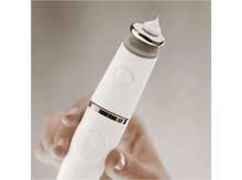 Charger l&#39;image dans la galerie, Un appareil de beauté blanc tenu par une main. Il y a une petite quantité de crème sur la pointe.
