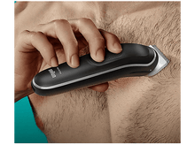 Charger l&#39;image dans la galerie, Une personne se rase les poils de la poitrine avec une tondeuse Braun noire. Gros plan sur la tondeuse et les poils.
