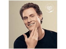 Charger l&#39;image dans la galerie, Un homme souriant et se touchant le visage. Il a les cheveux bruns et porte une chemise noire. Le fond est beige.
