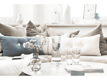 Charger l&#39;image dans la galerie, Carafe d&#39;eau avec des fleurs sur la table. Deux verres à droite. Canapé en arrière-plan.
