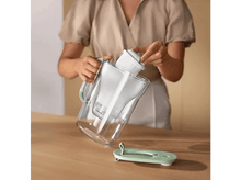 Charger l&#39;image dans la galerie, Une personne versant de l&#39;eau dans une carafe transparente, et un couvercle de filtre détaché sur une table.
