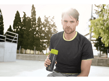Charger l&#39;image dans la galerie, Homme tenant une bouteille d&#39;eau, portant une chemise grise, debout dehors, avec des arbres en arrière-plan.
