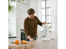 Charger l&#39;image dans la galerie, Un homme en pull marron fait de l&#39;eau gazeuse. Oranges et verre sur le comptoir en bois.

