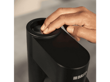 Charger l&#39;image dans la galerie, La main d&#39;une personne touchant un appareil de filtre à eau noir. L&#39;appareil a une ouverture circulaire.
