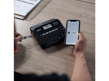 Charger l&#39;image dans la galerie, Une personne utilise une étiqueteuse Brother P-touch, un téléphone avec code-barres.
