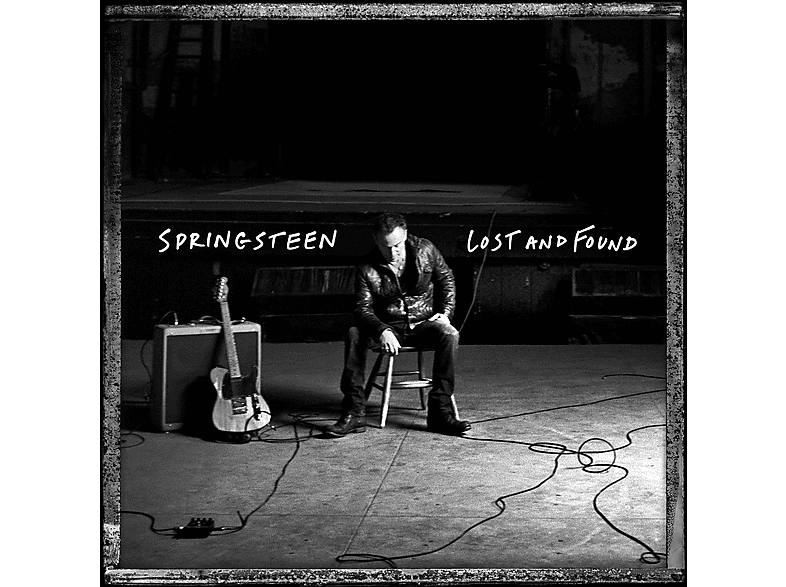 Photo en noir et blanc de Bruce Springsteen assis sur une chaise, guitare et ampli à côté de lui.