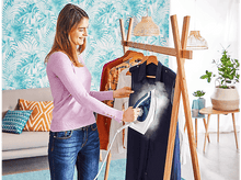 Charger l&#39;image dans la galerie, Une femme repasse une robe bleue suspendue sur un portant.
